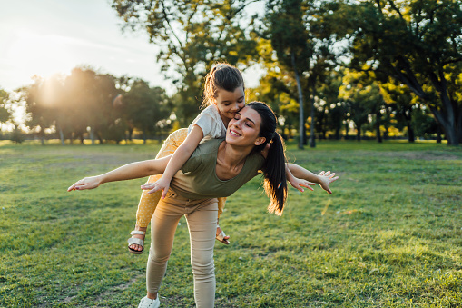 Cheerful mother and little daughter playing together in a public park