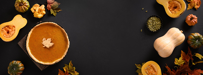 Autumn banner with American Pumpkin Pie and ingredients for homemade cooking on black background. View from above. Flat lay. Copy space.
