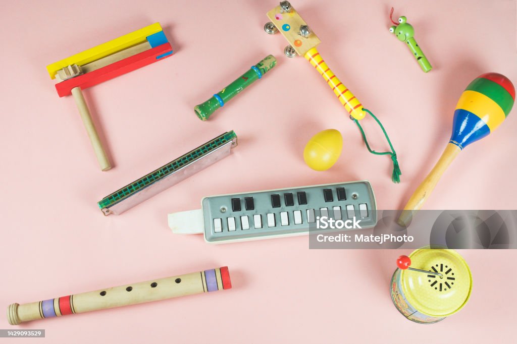 Wooden musical instruments for child. On the pink background. Colorful toys. Musical instruments toys for children. Wooden colorful whistles, rattle, percussion instrument, mouth harmonica organ and clacker in the kid's version. Funny child motif. Pink background. Art Stock Photo