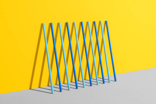 Eco friendly stripped paper straws stand leaning against the color wall. Ecology, recycling concept. Minimal geometric scene stock photo