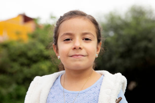 Portrait of a 10-year-old girl with a smiling and relaxed expression, wearing a white shirt against a white background.