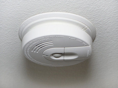 Closeup of a ceiling mounted white smoke detector used to activate warning systems in homes.