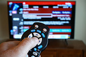 Hand using TV remote control with television out of focus