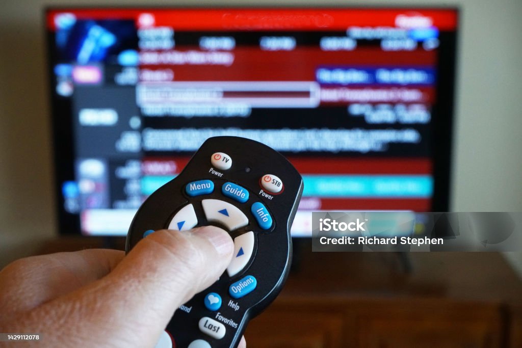 Hand using TV remote control with television out of focus Hand using a TV remote control with the television out of focus Live Streaming Stock Photo