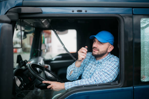 Driver using a radio in his truck Middle aged truck driver sitting in a cabin of his truck and using a radio semi truck audio stock pictures, royalty-free photos & images