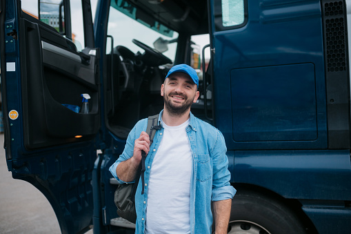 Portrait of a happy truck driver standing in front of his truck with his arms crossed, looking at the camera