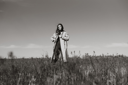 Black and white photo of Young woman stands in the dry grass reeds field looking away. Nature, fashion, vacation and lifestyle.