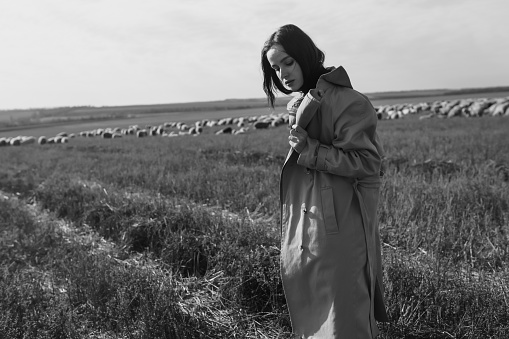 Black and white photo of Young woman stands in the dry grass reeds field looking away. Nature, fashion, vacation and lifestyle.
