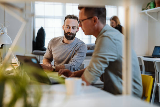 programmierer, die zusammenarbeiten und sich gegenseitig beim programmieren unterstützen. reife unternehmer, die im büro auf laptops arbeiten - computer programmer fotos stock-fotos und bilder