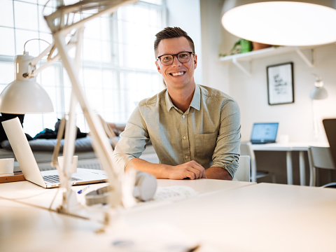 Emprendedor adulto medio que trabaja en una computadora portátil en una oficina de espacio abierto. Hombre de negocios mirando a la cámara y sonriendo photo