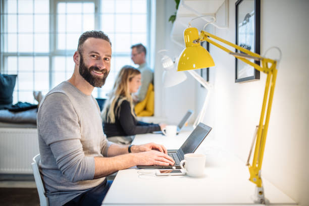 istock Mature programmer working on laptop in co-working space. Bearded employee smiling and looking at camera 1429126029