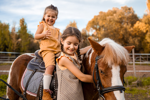 Two little girls riding and petting a pony