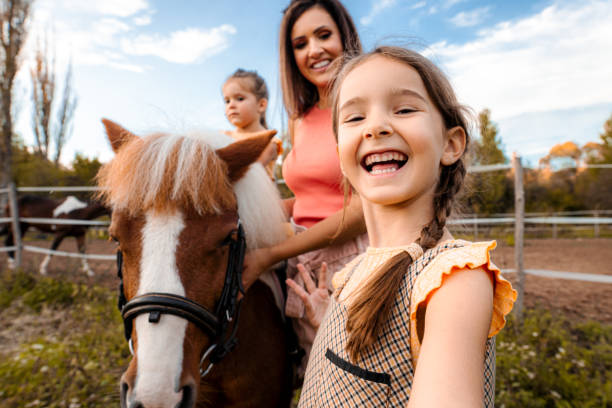 мать с двумя маленькими дочерьми на конном ранчо - horse child pony little girls стоковые фото и изображения