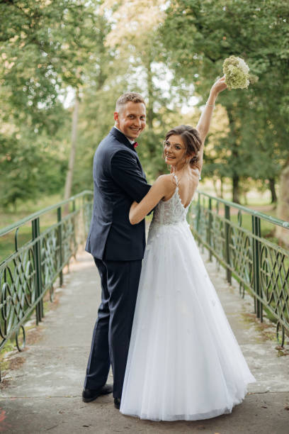 istock Glad smiling wedding couple standing on bridge in park in summer, looking back. Young bride preparing to throw bouquet. 1429131108