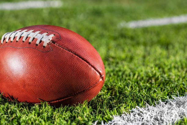 A close-up of an American football sitting next to a white yard line with hash marks stock photo