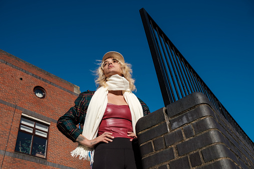 Portrait of modern alternative young woman posing in an urban environment in a sunny day. She is looking away and she wears scarf and leather top.