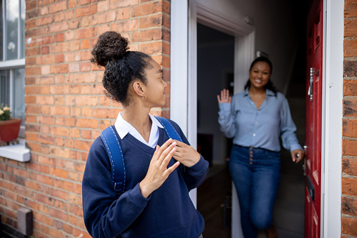 Black girl going to school and waving goodbye to her mother - education concepts
