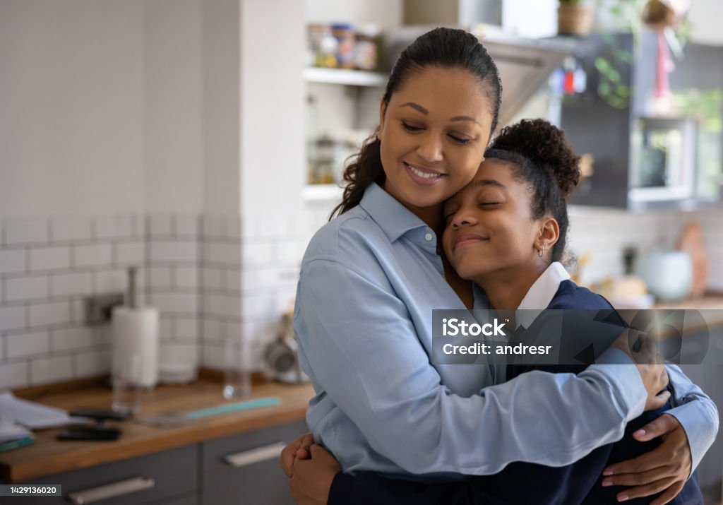 Loving mother hugging her daughter after she arrives home from school Loving mother hugging her daughter after she arrives home from school - domestic life concepts Parent Stock Photo