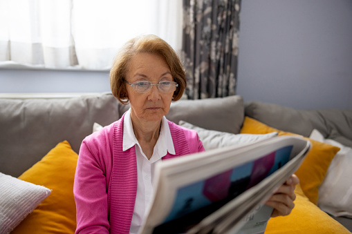 Senior woman reading the newspaper at home wearing reading glasses -retirement lifestyle concepts