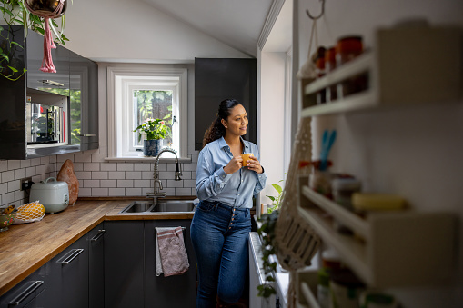 Woman relaxing at home drinking a cup of coffee and looking through the window - lifestyle concepts