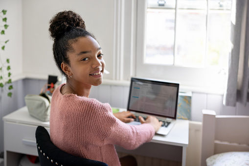 Happy teenager girl at home working on her laptop in her bedroom and doing her homework   lifestyle concepts