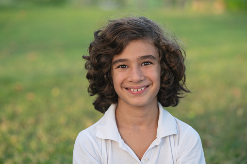 Head and shoulders portrait of 9 years old boy under day light. He is looking at camera and wearing a white colored t-shirt. Shot outdoor with a full frame mirrorless. camera.