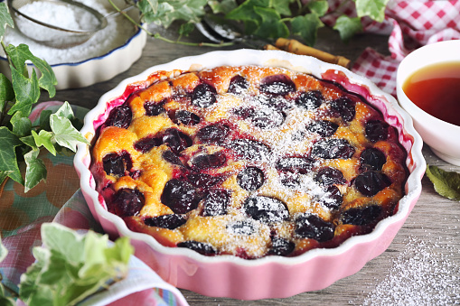 Blue plum clafoutis (flan), icing sugar dressing and cup of tea, french cuisine on wooden background