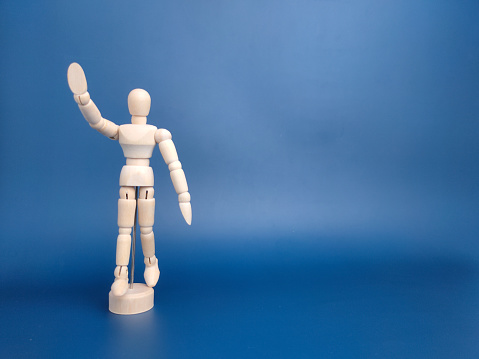 Wooden mannequin holding blank smartphone with white screen space for copy text and isolated on blue background.