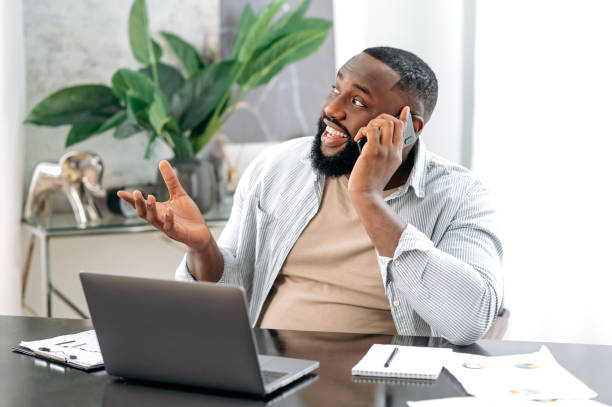 istock Cell Phone conversation. Positive african american man having smartphone negotiation during work time with client or coworker while sitting on his workplace in the office, smiling, gesticulation hand 1429168357