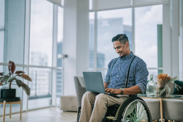 azjatycki indyjski projektant z niepełnosprawnością na wózku inwalidzkim korzystający z laptopa w salonie biznesowym - technology typing male beauty asian and indian ethnicities zdjęcia i obrazy z banku zdjęć