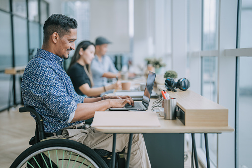 Trabajador indio asiático de cuello blanco en silla de ruedas concentrado trabajando en la oficina junto a su colega photo