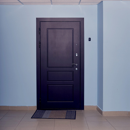 Dark brown door in the entrance of an apartment building with blue corridor walls