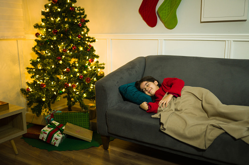 Happy little kid smiling while sleeping waiting for the presents from santa next to the christmas tree