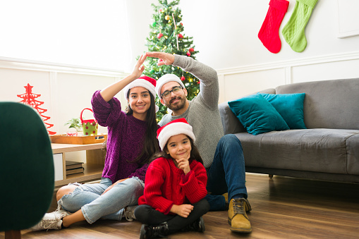 Beautiful parents and young child making a home gesture and enjoying a family christmas