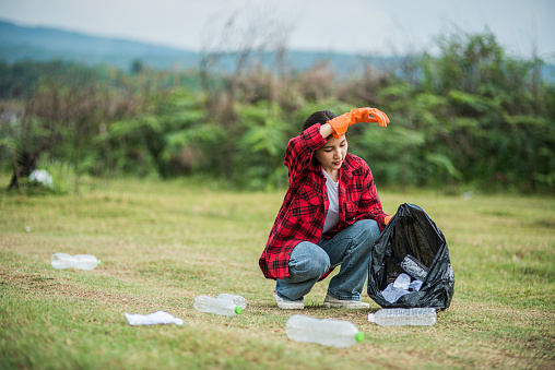 Woman wearing orange gloves collecting garbage in a black bag.