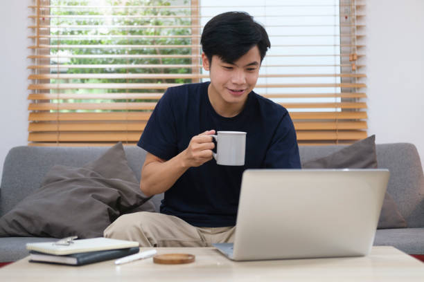 istock Handsome asian man sitting on couch and using laptop, browsing internet, replies to email, working online. 1429225018