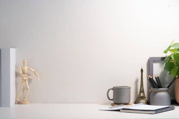 istock Minimal workplace with empty picture frame, book, coffee cup and pencil holder on white table. Copy space for your text. 1429234870