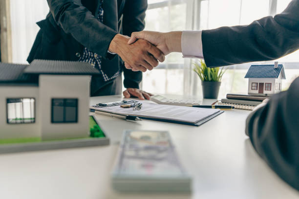 istock A real estate agent shakes hands with a client after completing a transaction regarding a house contract agreement. Contract documents and a house model on a wooden table. 1429238144