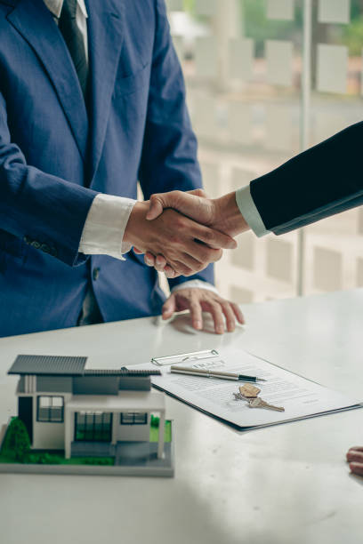 istock A real estate agent shakes hands with a client after completing a transaction regarding a house contract agreement. Contract documents and a house model on a wooden table. 1429238245