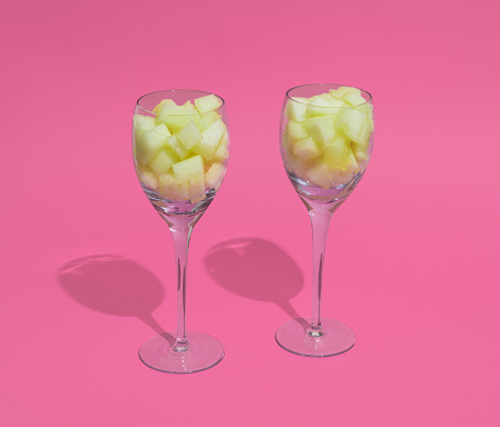 Luxury glasess filled with Honeydew melon cubes on a pink background. Minimal square composition, healthy sweet food serving concept