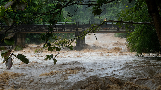 Waterfall cataract in forest mountains. Dirty streams are flowing down the mountain slopes of the mountain forest after heavy rains in Thailand. River flood, selective focus.