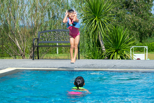 Happy little sisters play in outdoor swimming pool of tropical resort during family summer vacation. Kids learning to swim. Healthy Summer Activities for Kids.