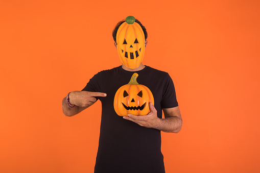 Person with pumpkin mask celebrating Halloween, holding and pointing at a pumpkin. Concept of celebration, All Souls' Day and All Saints' Day.