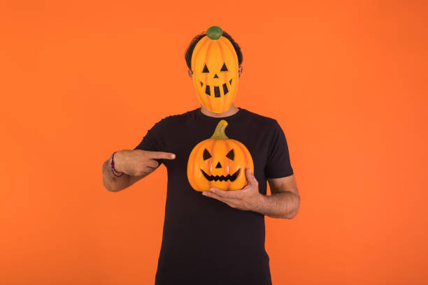 Person with pumpkin mask celebrating Halloween, holding and pointing at a pumpkin. Concept of celebration, All Souls' Day and All Saints' Day. stock photo