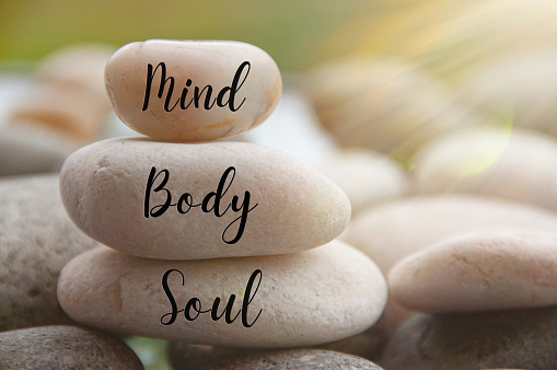 Light shining on zen stones with words Mind, Body, Soul on blurred background. Customize space for text or ideas.