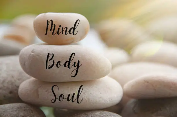 Photo of Light shining on zen stones with words Mind, Body, Soul on blurred background. Customize space for text or ideas