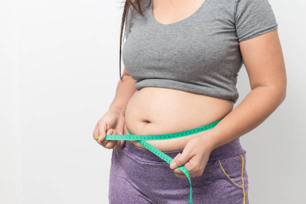 Overweight woman check out his body fat with green measuring tape for obesity on gray background, Healthy concept stock photo