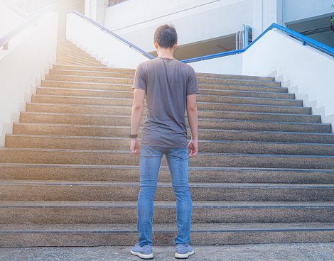 A young man, good figure, tall and wearing a t-shirt, jeans, was about to go up the stairs. Walk up the stairs where the light shines down.