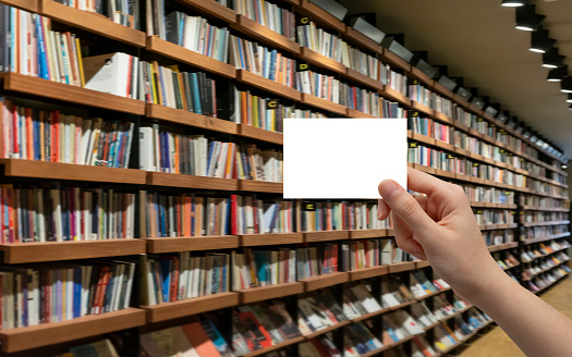 hand holding white card in front of bookshelf