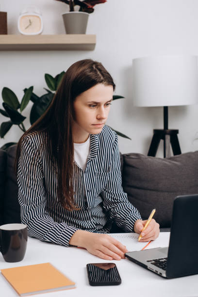 istock Thoughtful woman working holding pen making notes in diary sit on sofa at home. Startup and small business concept. Portrait of young pensive female using laptop staying online indoors artisan 1429261139